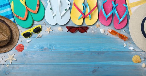 Photo of Many different flip flops and beach objects on light blue wooden background, flat lay. Space for text