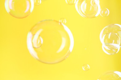 Photo of Beautiful transparent soap bubbles on yellow background