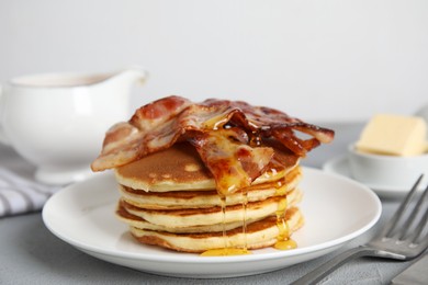 Photo of Delicious pancakes with maple syrup and fried bacon on grey table, closeup