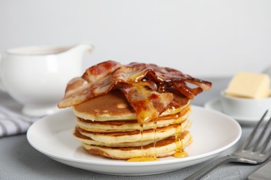 Delicious pancakes with maple syrup and fried bacon on grey table, closeup