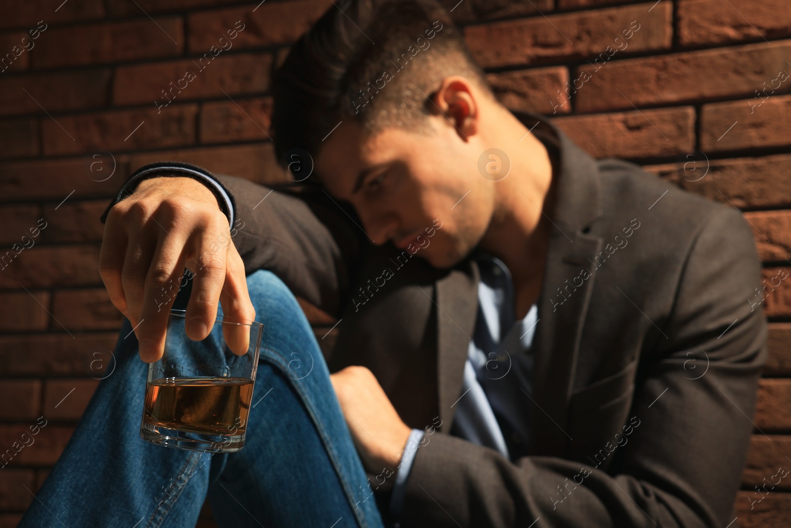 Photo of Addicted man near red brick wall, focus on glass of alcoholic drink