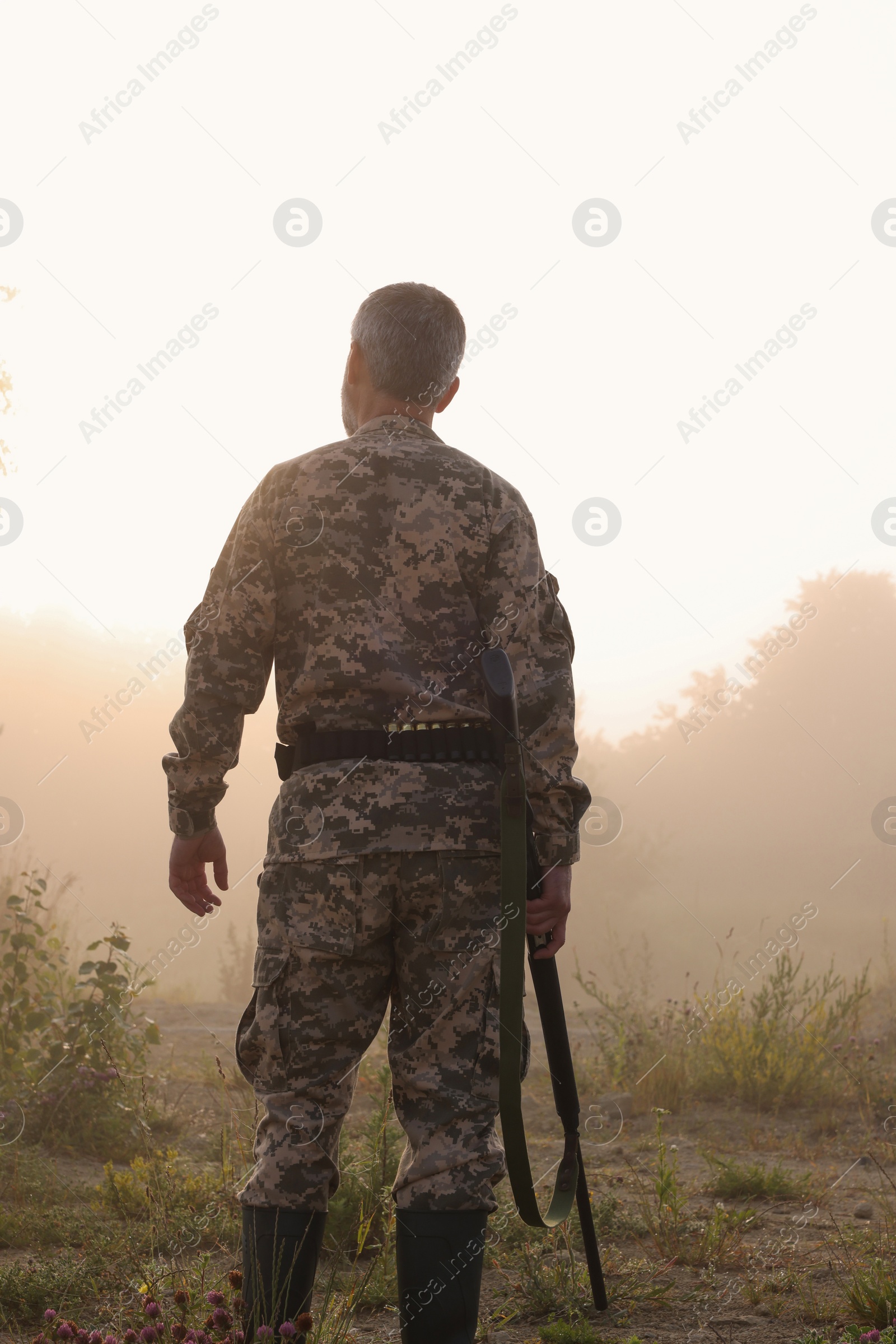 Photo of Man with hunting rifle wearing camouflage outdoors, back view