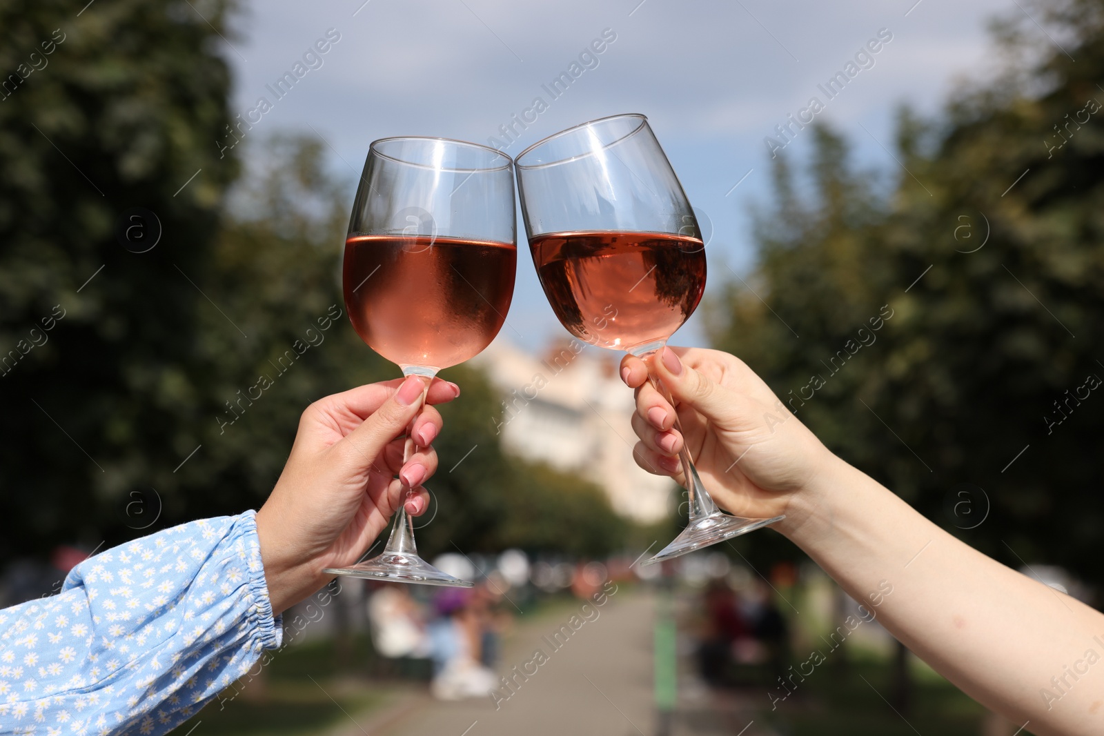 Photo of Women clinking glasses with rose wine outdoors, closeup