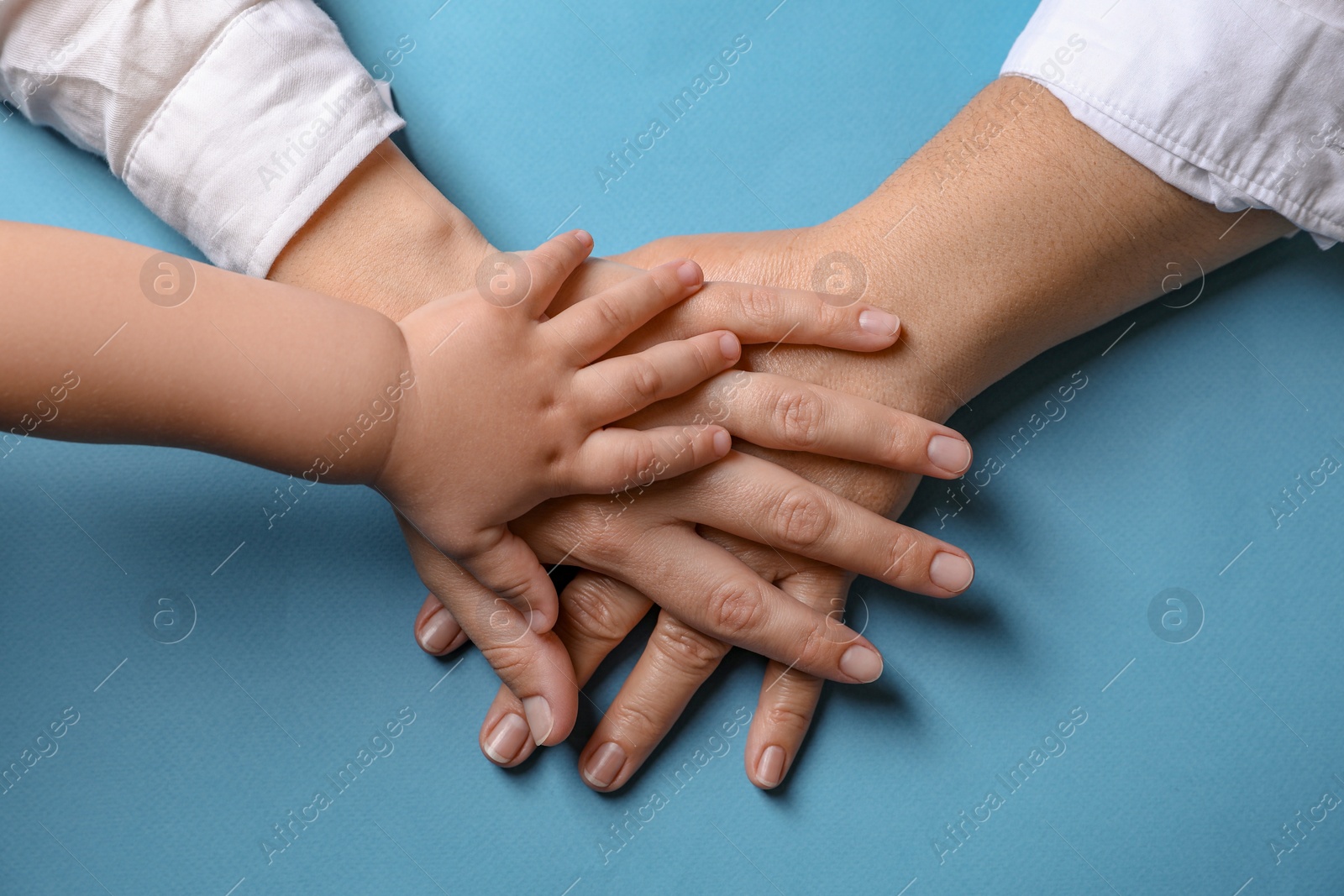 Photo of Family holding hands together on light blue background, top view