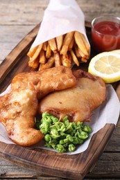 Photo of Tasty fish, chips, sauce and peas on wooden table, closeup