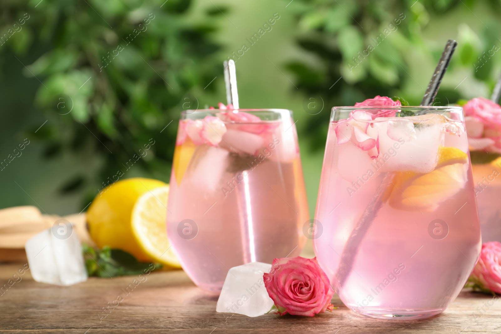 Photo of Delicious refreshing drink with rose flowers and lemon slices on wooden table, closeup