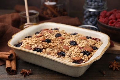 Photo of Tasty baked oatmeal with berries, almonds and spices in baking tray on wooden table, closeup