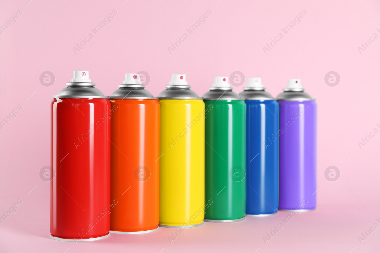 Photo of Colorful cans of spray paints on pink background