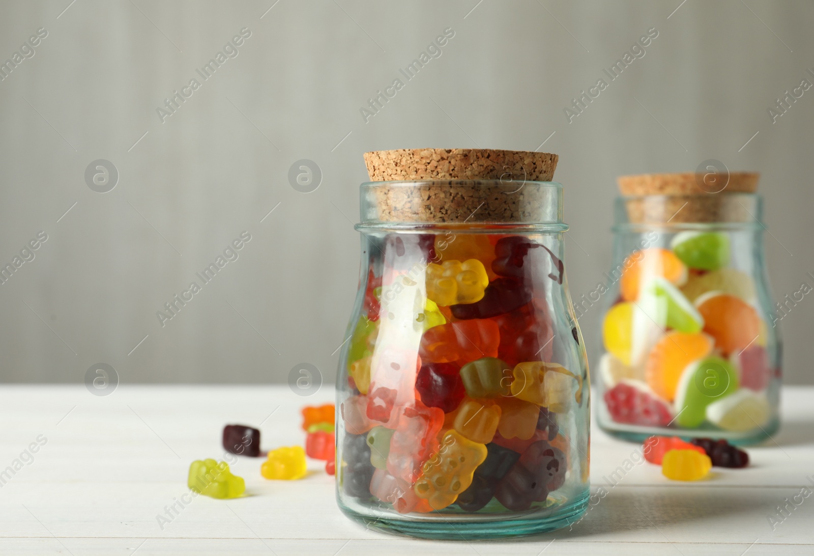 Photo of Delicious gummy candies in glass jar on white wooden table