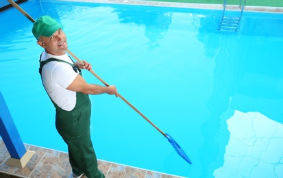 Male worker cleaning outdoor pool with scoop net