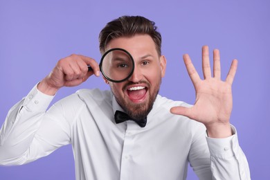 Photo of Emotional man looking through magnifier on violet background