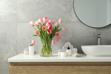 Vase with beautiful pink tulips and toiletries near sink in bathroom