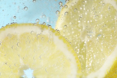 Photo of Juicy lemon slices in soda water against light blue background, closeup