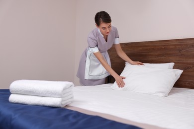 Beautiful chambermaid making bed in hotel room