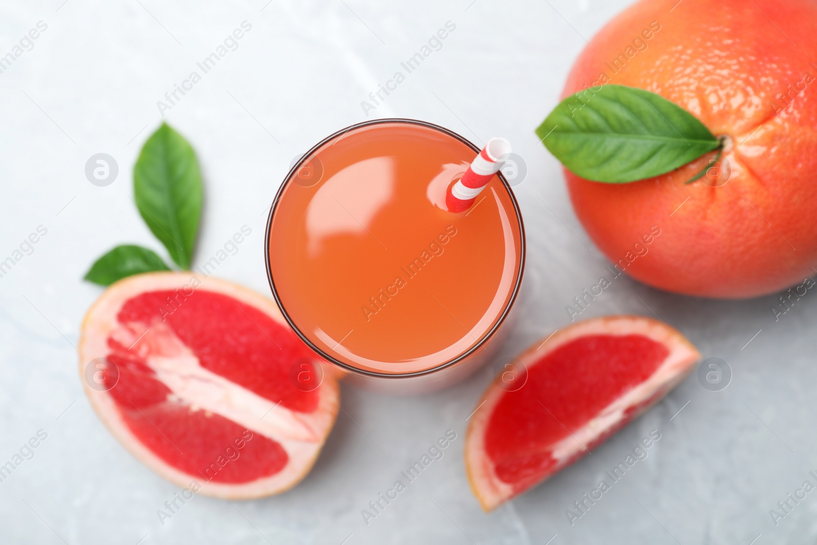 Photo of Tasty freshly made grapefruit juice and fruits on light grey marble table, flat lay 