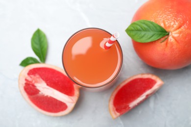 Photo of Tasty freshly made grapefruit juice and fruits on light grey marble table, flat lay 