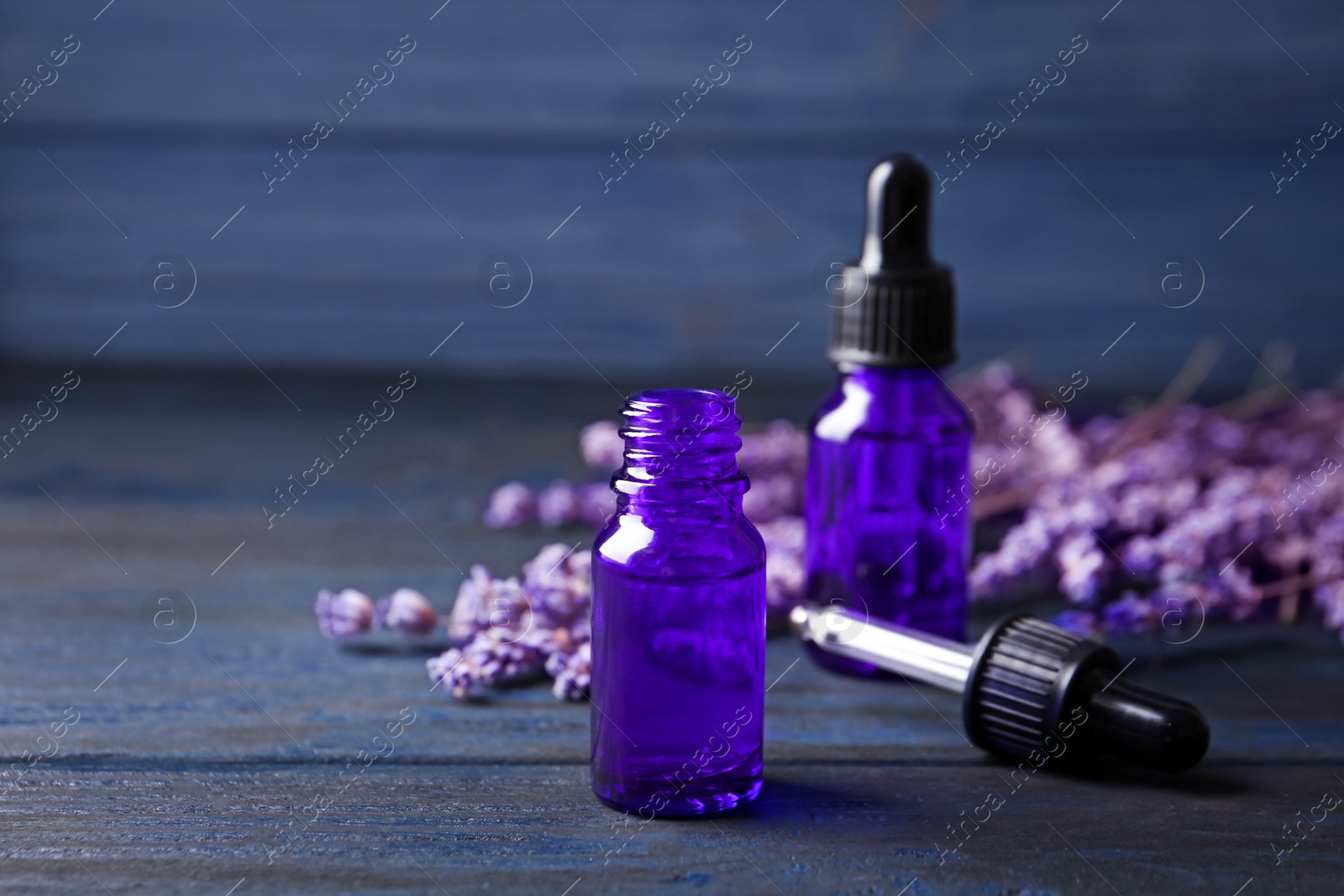 Photo of Bottles of lavender essential oil on blue wooden background