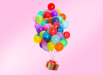 Many balloons tied to gift box on pink background