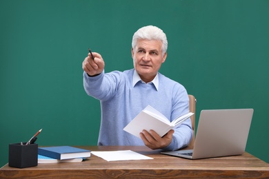 Photo of Portrait of senior teacher with laptop at table against green chalkboard