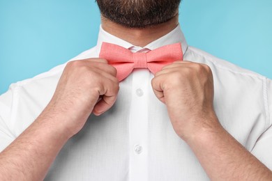 Photo of Man in shirt adjusting bow tie on light blue background, closeup