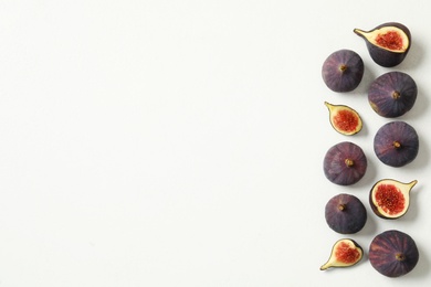 Photo of Whole and cut tasty fresh figs on white table, flat lay. Space for text