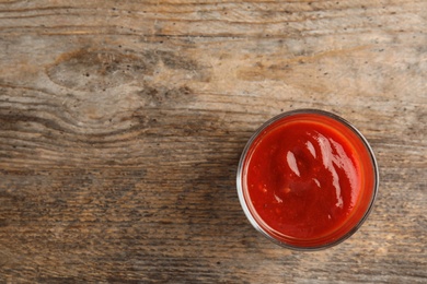 Photo of Glass of tasty tomato sauce on wooden table, top view. Space for text