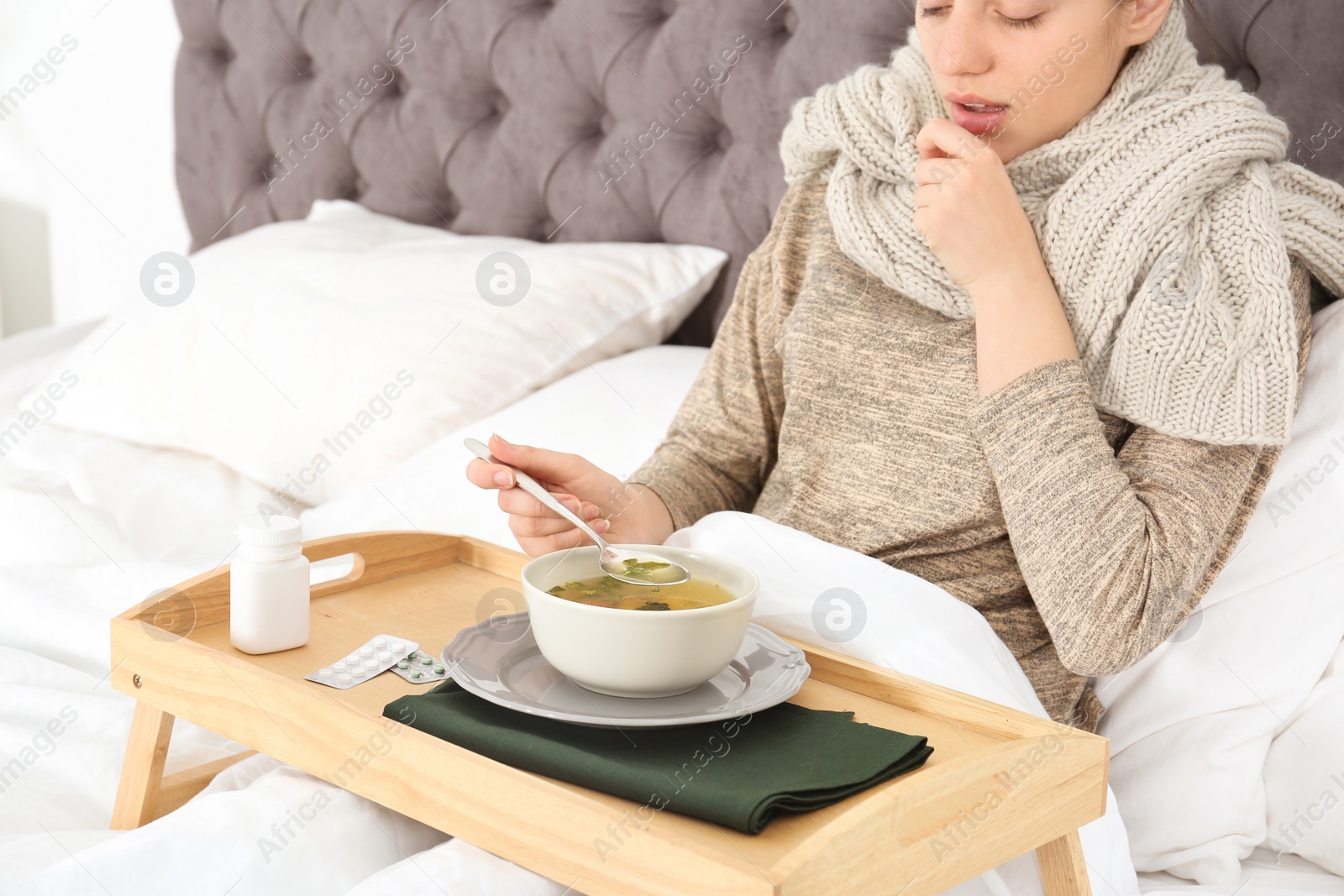 Photo of Sick young woman eating broth to cure cold in bed at home