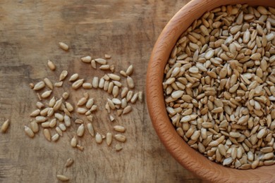 Bowl and organic sunflower seeds on wooden table, flat lay