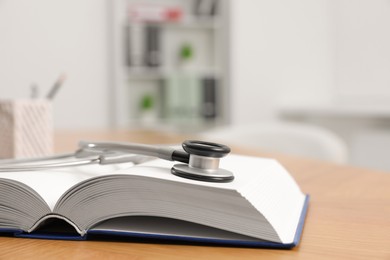 Photo of Book and stethoscope on wooden table in clinic, closeup. Space for text