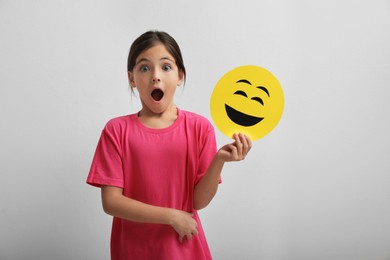 Photo of Shocked little girl holding face with laughing emoji on white background