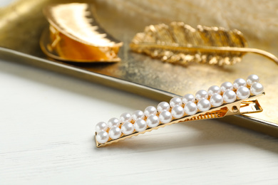 Photo of Stylish hair clips and gold tray on white wooden table
