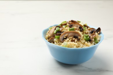 Photo of Delicious bulgur with mushrooms and green onion in bowl on white marble table, closeup. Space for text