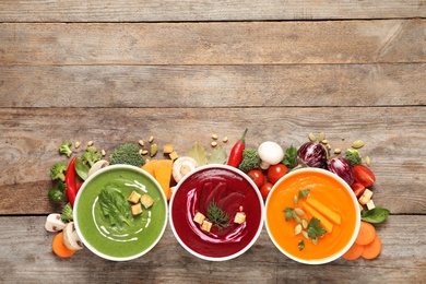 Various cream soups, ingredients and space for text on wooden background, flat lay. Healthy food