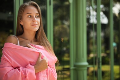 Photo of Beautiful young woman in stylish pink shirt near building outdoors, space for text