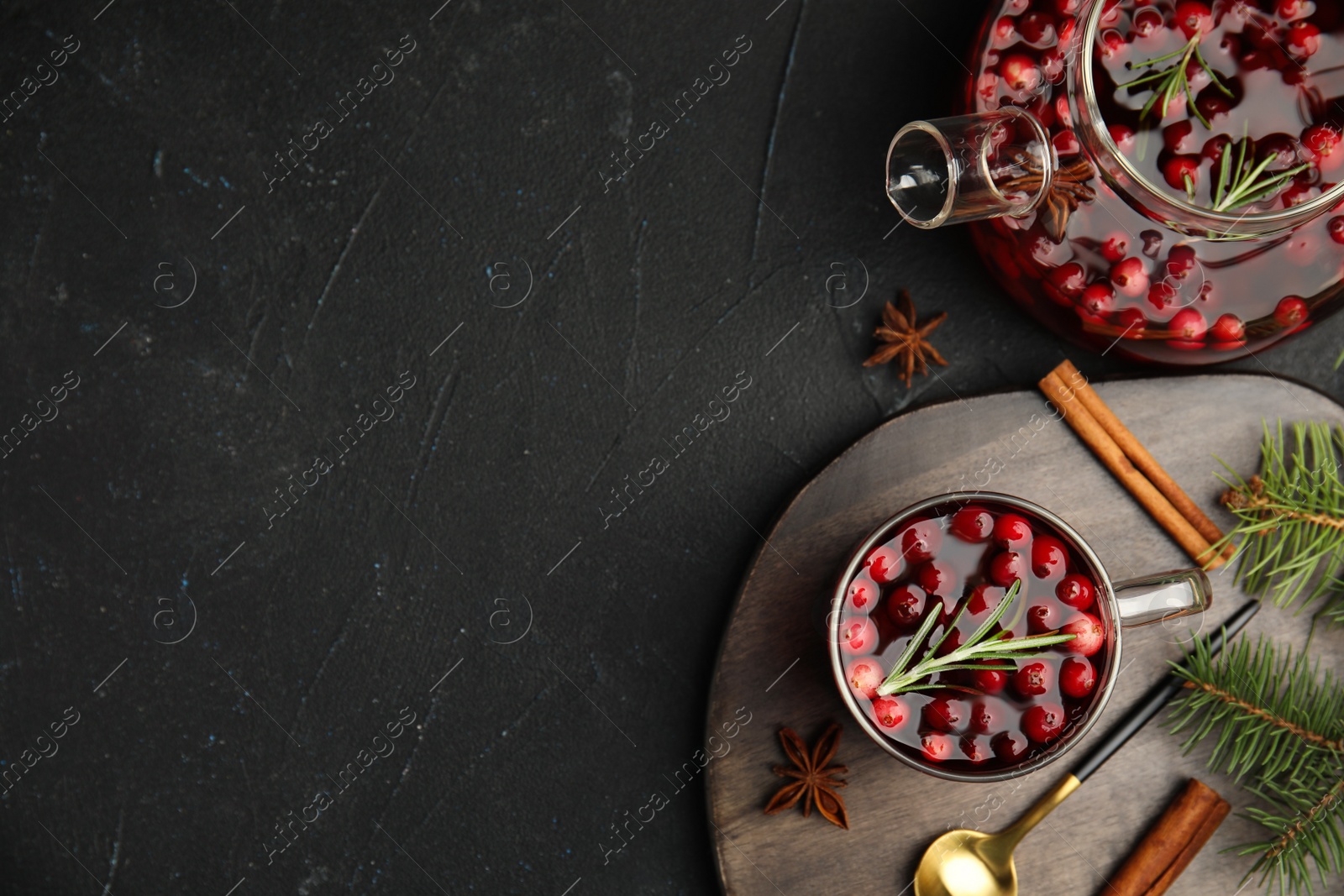 Photo of Tasty hot cranberry tea with rosemary, anise and cinnamon on black table, flat lay. Space for text