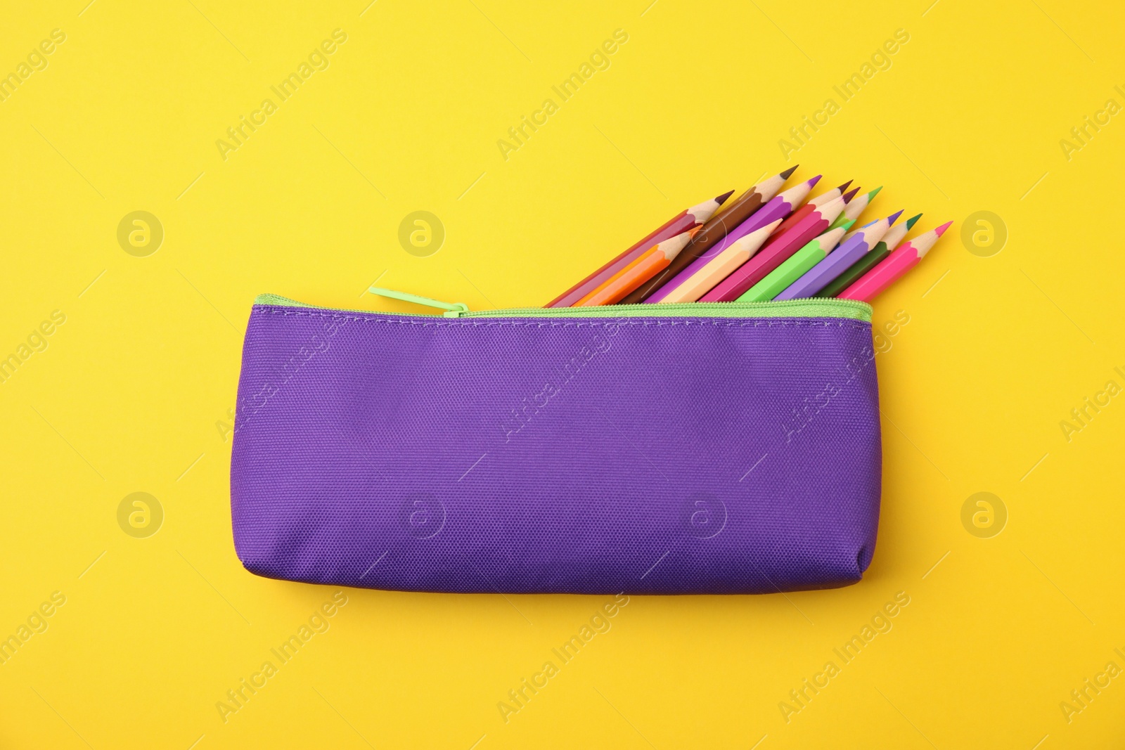 Photo of Many colorful pencils in pencil case on yellow background, top view