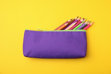 Many colorful pencils in pencil case on yellow background, top view