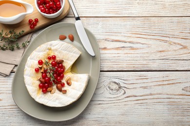 Photo of Brie cheese served with almonds, red currants and honey on white wooden table, flat lay. Space for text