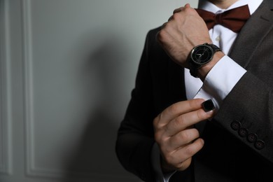 Man wearing stylish suit and cufflinks near white wall, closeup. Space for text