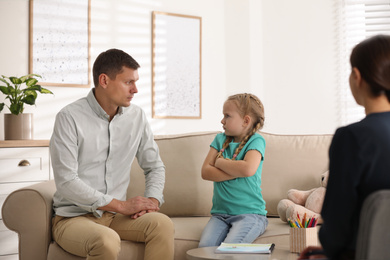Photo of Little girl and her father on appointment with child psychotherapist indoors