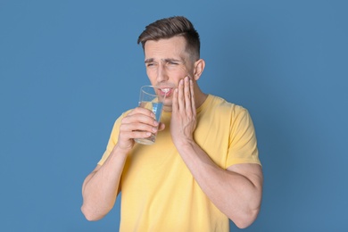 Photo of Young man with sensitive teeth and glass of cold water on color background
