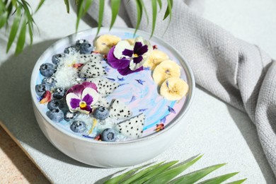 Photo of Delicious smoothie bowl with fresh fruits, blueberries and flowers on color textured table, closeup