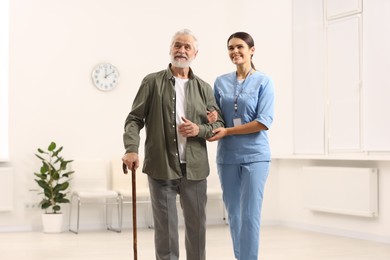 Photo of Smiling nurse supporting elderly patient in hospital