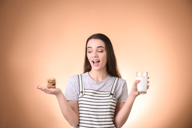 Photo of Beautiful young woman drinking milk with cookies on color background