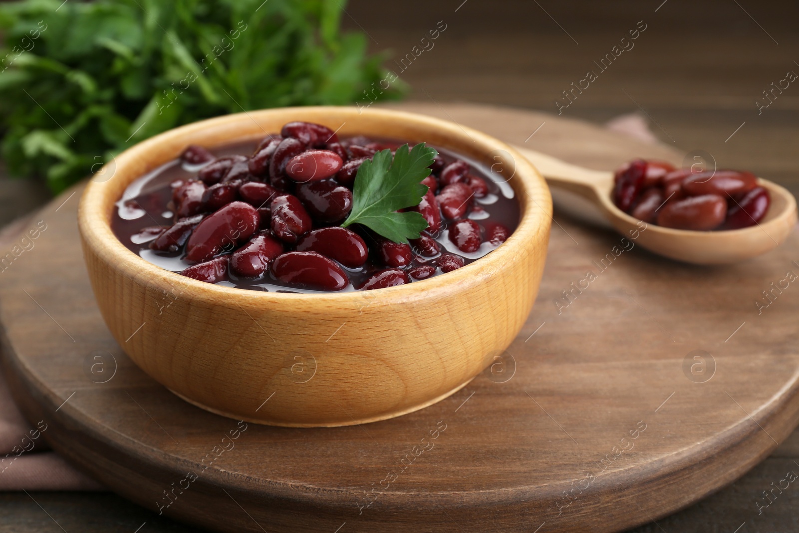 Photo of Bowl of canned red kidney beans with parsley on wooden table, closeup