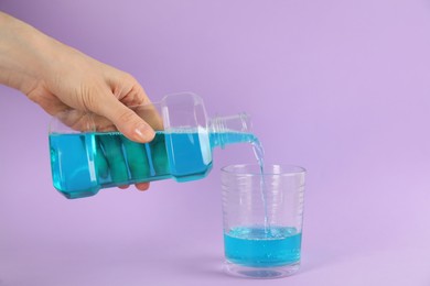 Photo of Woman pouring mouthwash into glass on violet background, closeup