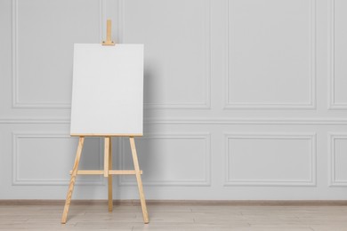 Photo of Wooden easel with blank canvas near white wall indoors. Space for text