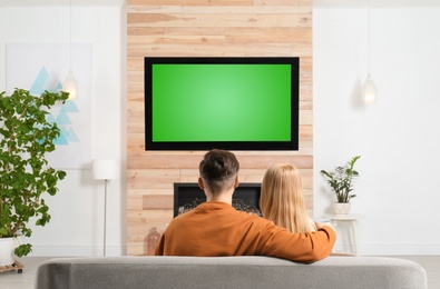 Photo of Couple watching TV on sofa in living room with decorative fireplace