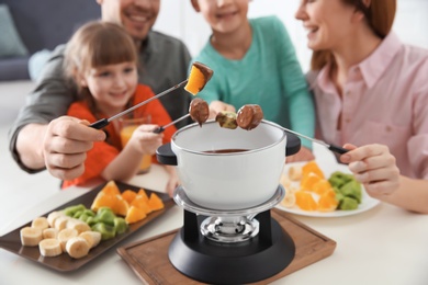 Photo of Happy family enjoying fondue dinner at home, closeup