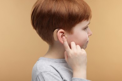 Little boy with hearing aid on pale brown background
